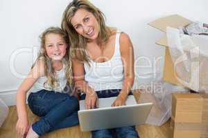 Mother and daughter sitting on the floor and using laptop