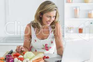 Woman using laptop while preparing vegetables