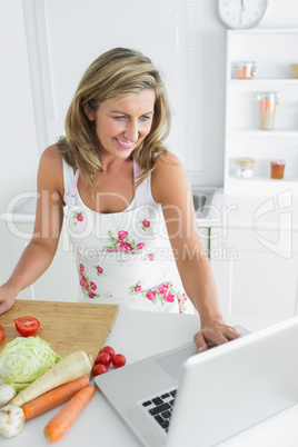 Smiling woman using laptop while preparing vegetables