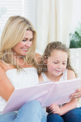 Mother and daughter sitting on the sofa with a book