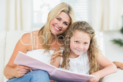 Mother and daughter sitting on the sofa with a book