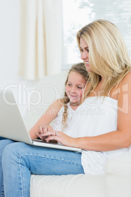 Woman typing on notebook while her daughter is sitting next to h