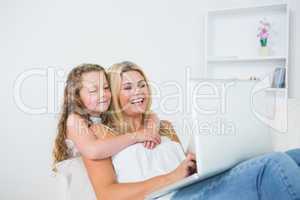 Daughter hugging mother whose working on laptop