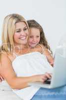 Mother using laptop with her daughter leaning on her shoulder