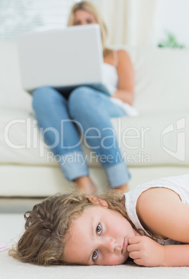 Daughter resting on the floor while her mother using notebook