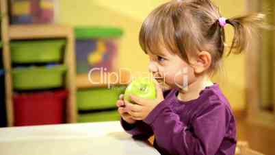 Babies and food, female child eating green apple in kindergarten