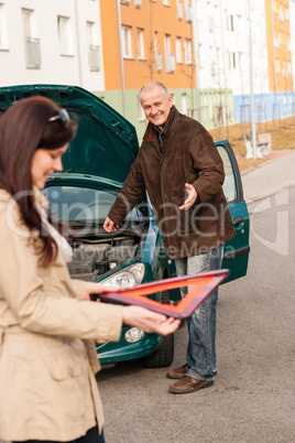 Woman holding triangle sign repairman fixing car