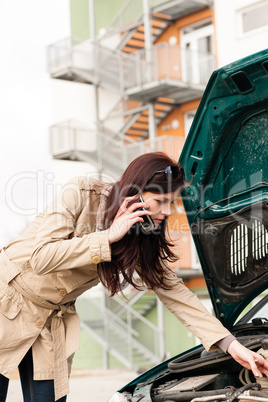 Woman looking under car hood on phone