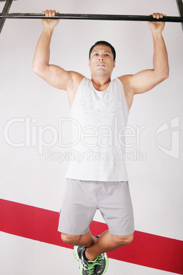 Strong man doing pull ups on a bar in a gym in the background.