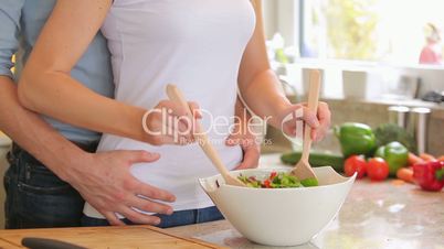 Woman mixing salad with man holding her from behind