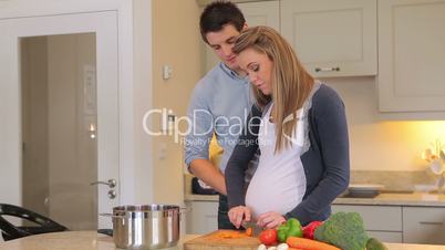 Pregnant wife cutting vegeatables and eating them with husband