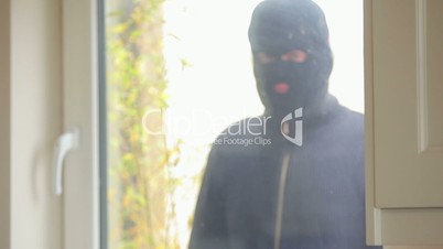 Burglar looking through the window at woman on laptop