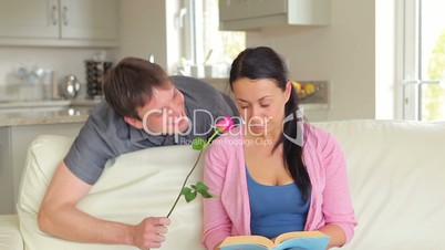 Woman reading book is surprised by husband with flower