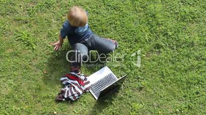 Boy sitting at laptop, outdoors, on the lawn