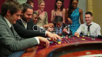 Men placing bets at roulette table watched by women