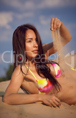 A girl in a bikini lies on sand