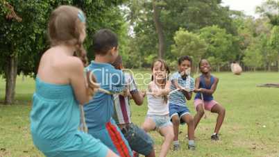 Happy school children playing tug of war in park