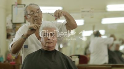 Old man cutting hair to client in men's beauty parlor