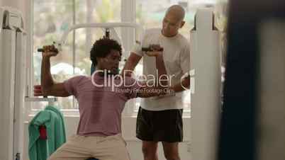 Personal trainer helping man working out in fitness gym