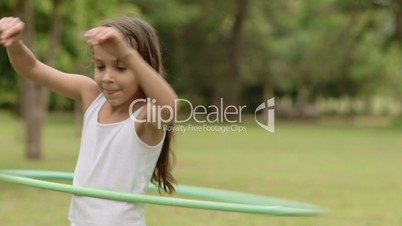 Happy young girl playing with hula-hoop in park