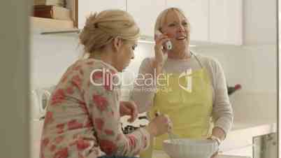 Mom and daughter cooking in home kitchen, talking on telephone