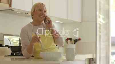 Retired woman speaking on telephone and preparing food at home