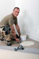 Smiling carpet fitter spreading adhesive on an old tiled floor