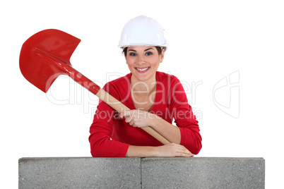 Girl with shovel leaning on a brickwall