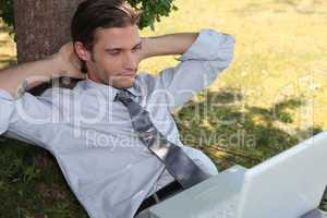 Young man relaxing in the grass with laptop