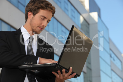 Young executive using a laptop outside an office building