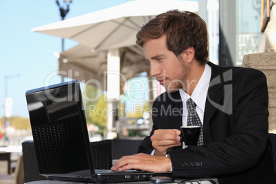 business man drinking coffee and watching his laptop on a street cafe