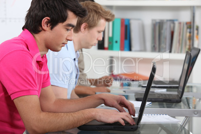 young male students in class working on laptops