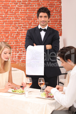 Waiter stood by couple enjoying meal