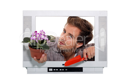 man holing flowerpot and a trowel looking through a television frame