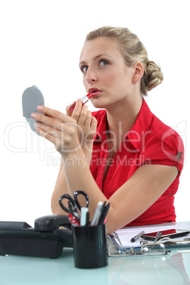 Blond secretary applying lip-stick at her desk