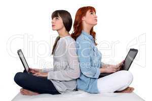 Two female friends sat together each using a laptop computer