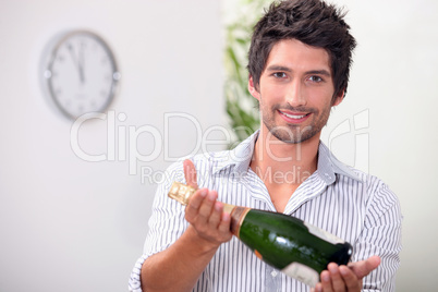 Man offering a bottle of champagne at five minutes to midnight