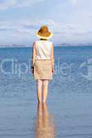 Woman with hat standing in the sea and looks into the distance