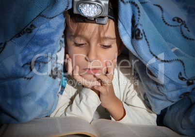 Boy reading a book under the covers with a flashlight