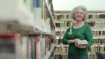 Happy senior woman reading and choosing book in library