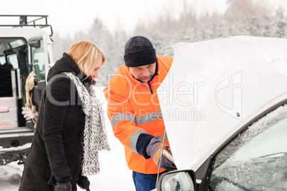 Woman mechanic looking under car hood snow