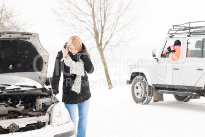 Woman looking under broken car hood snow