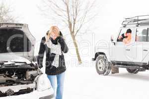 Woman looking under broken car hood snow