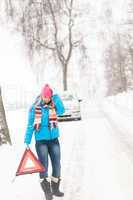 Woman with warning triangle car snow breakdown