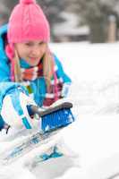 Woman wiping car windshield using brush snow