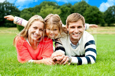 Couple lying in park with their daughter on top