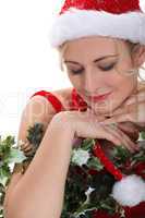 blonde woman wearing a Christmas costume hugging holly and having an expression of purity