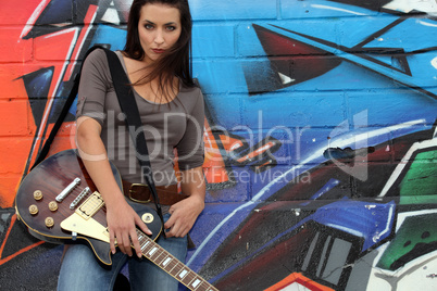 Female guitarist stood by graffiti