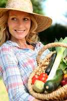 Woman with a straw hat holding basket of vegetables.
