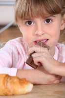 Little girl eating chocolate bar for breakfast